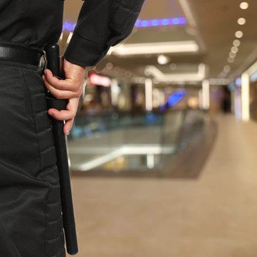 Security guard in uniform with police baton in shopping mall, closeup. Space for text