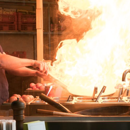 Cook is fry vegetables with spices and sauce in a wok on a flame. Cooking process in an Asian restaurant.