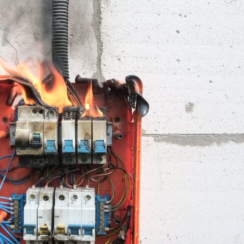 Burning switchboard from overload or short circuit on wall. Circuit breakers on fire and smoke from overheating due to poor connection. Dangerous home electrical wiring concept, copy space
