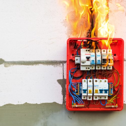 Burning switchboard from overload or short circuit on wall. Circuit breakers on fire from overheating due to poor connection or poor quality wires. Dangerous home electrical wiring concept