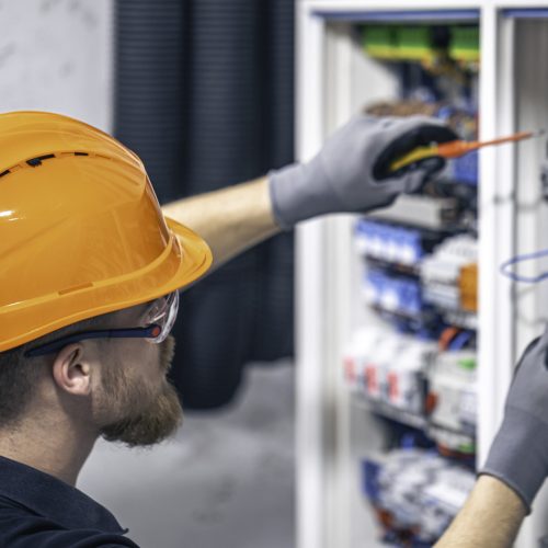 A male electrician works in a switchboard with an electrical connecting cable.