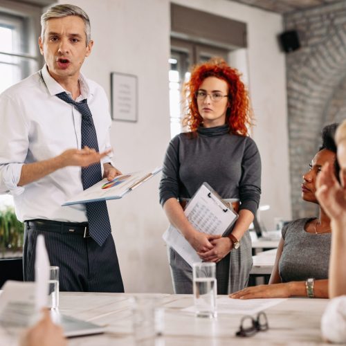 Angry businessman feeling disappointed with business reports and scolding his team during a meeting in the office.